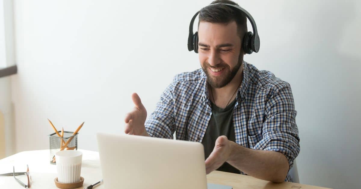 Bearded man with headphones gesturing to his laptop as if having a conversation