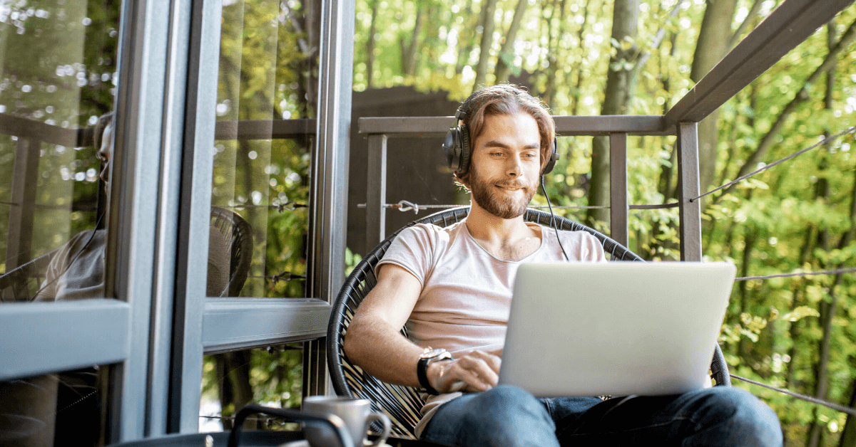 Software developer sitting outside on balcony working in front of his laptop with headphones