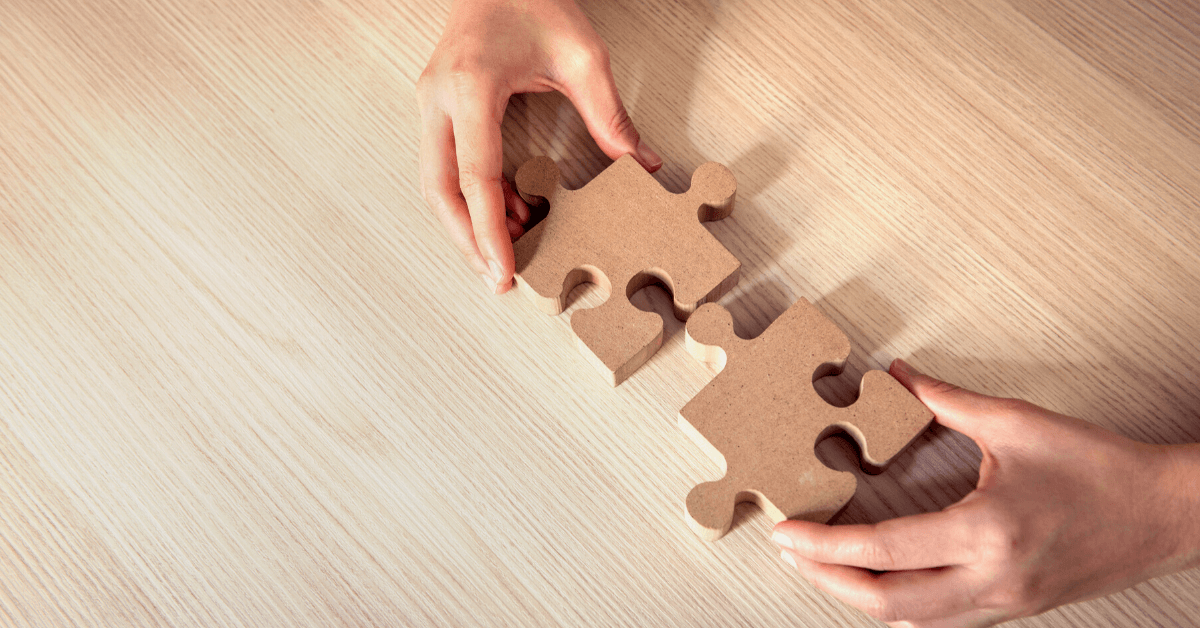 hands fitting together wooden puzzle pieces over wooden desk