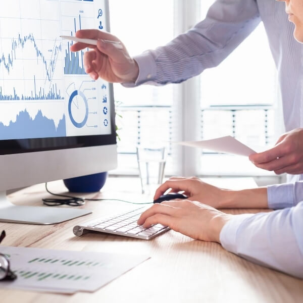 Two people sitting in front of a computer looking at graphs and reports on the screen.